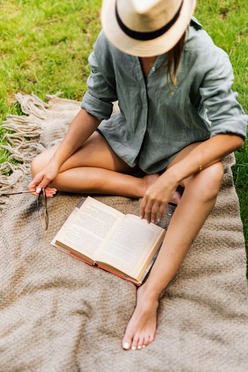 Free Woman relaxing outdoors with a book and hat, enjoying a tranquil summer day. Stock Photo