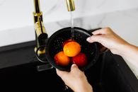 Person Holding Red Tomato in Black Steel Cooking Pot