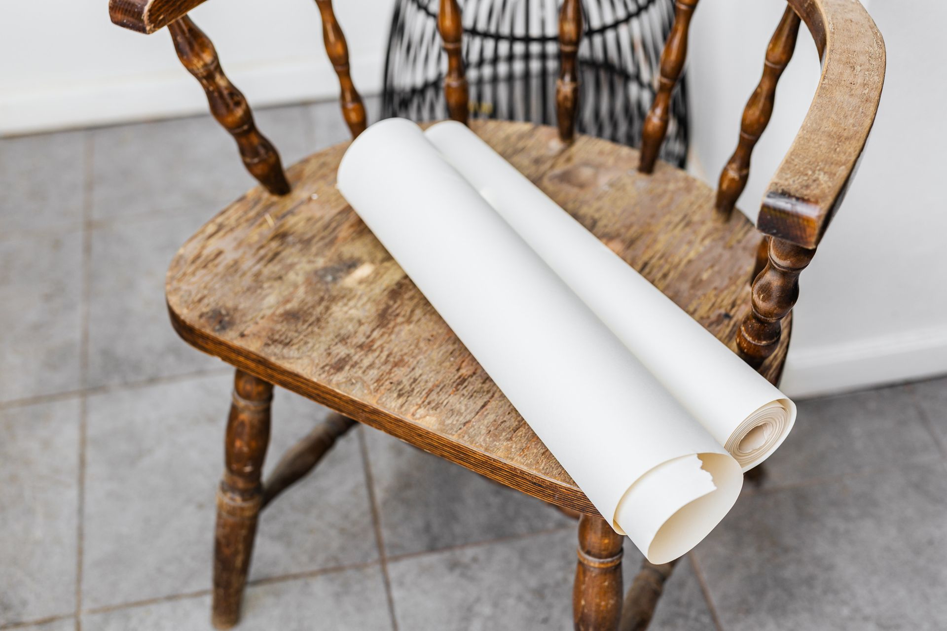 An antique wooden chair with rolled paper on a tiled indoor floor, capturing a vintage essence.