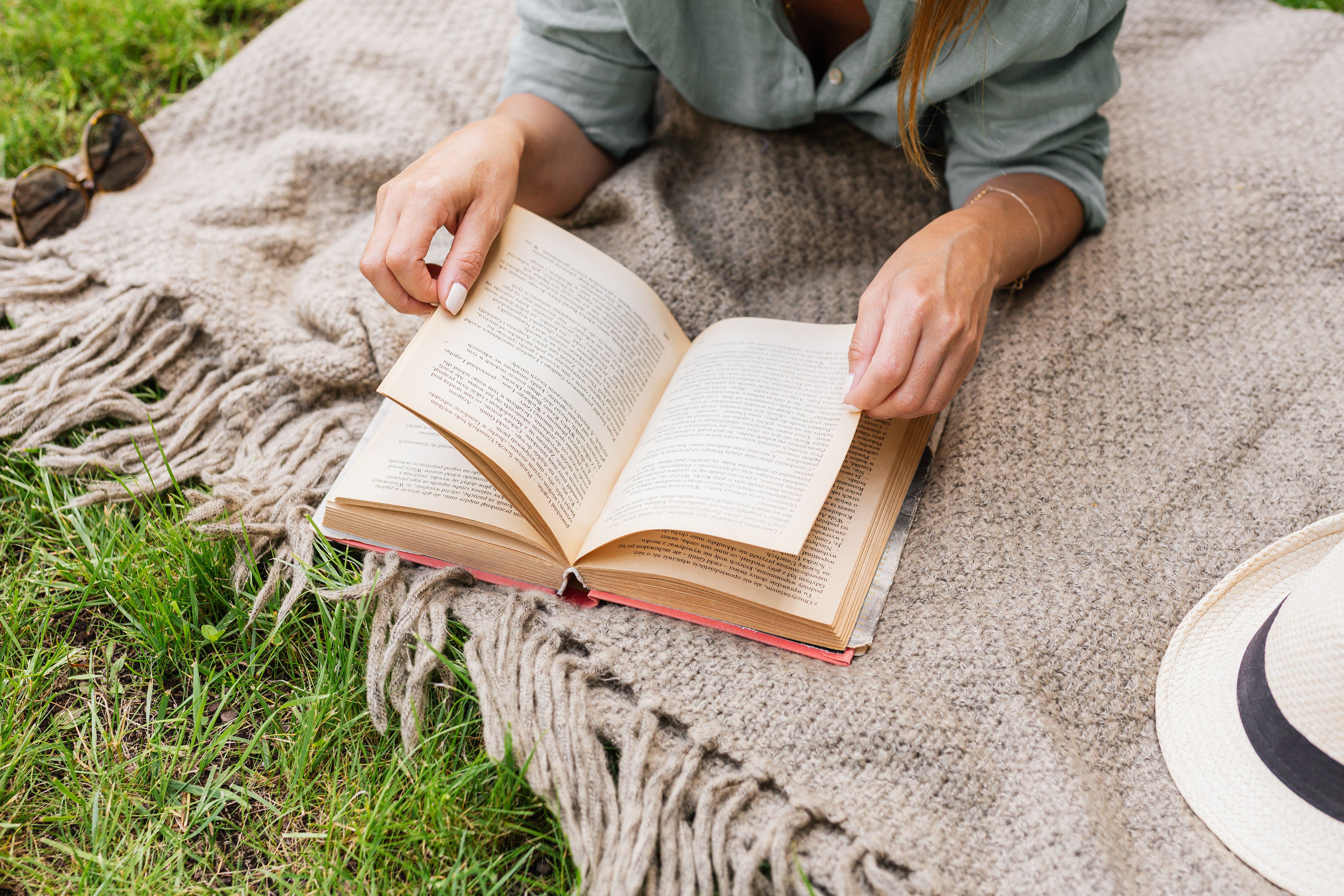 A woman enjoys a peaceful moment reading a book on a cozy blanket outside