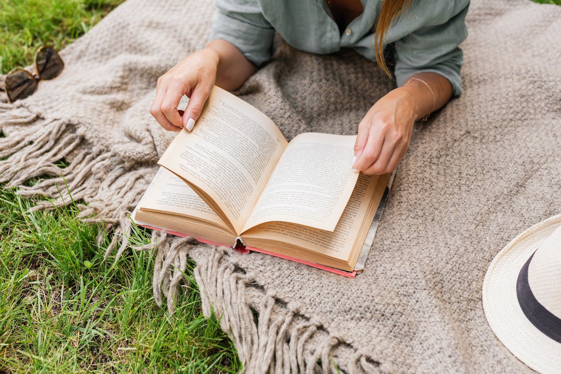 Close-up of Woman on Blanket Reading Book Outdoors · Free Stock Photo