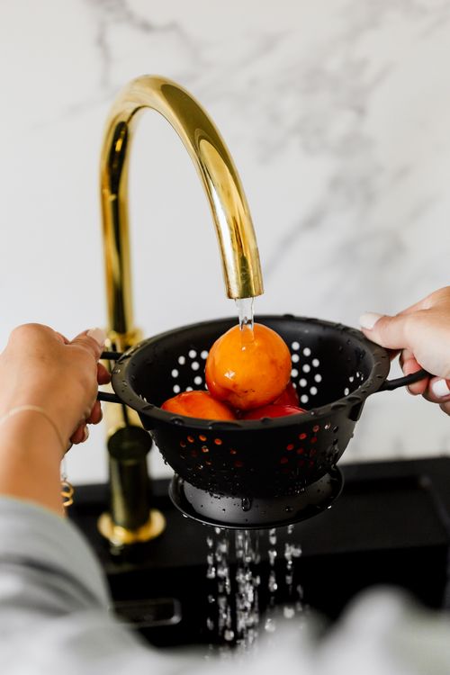 Free Close-up of hands washing oranges in a black colander under a gold faucet. Stock Photo