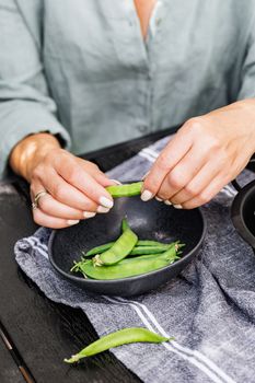 一个女人在厨房的毛巾上剥豌豆，碗放在旁边