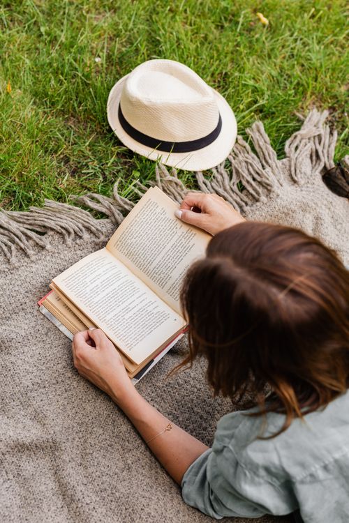 Free A woman enjoys reading on a picnic blanket in the grass on a sunny day. Stock Photo