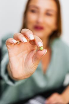 焦点中，一位模糊的女人拿着一颗绿色小药丸；这是关于健康和医学的概念