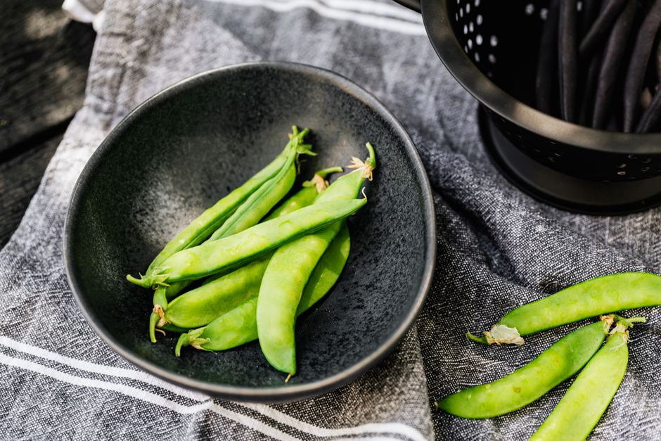 A bowl of tan dried pigeon peas next to a handful of fresh green pigeon pea pods split open to show the peas inside