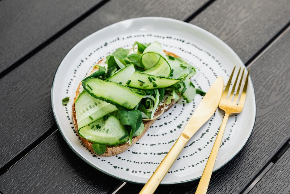 A close-up of a healthy open-faced sandwich with cucumber and greens on a patterned plate.