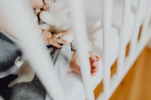 Adorable baby sleeping peacefully in a crib, holding a soft toy next to a baby blanket.