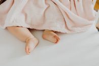 白色床上柔软的粉红色毯子下，露出了可爱新生婴儿的小脚