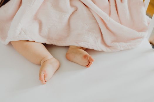 白色床上柔软的粉红色毯子下，露出了可爱新生婴儿的小脚