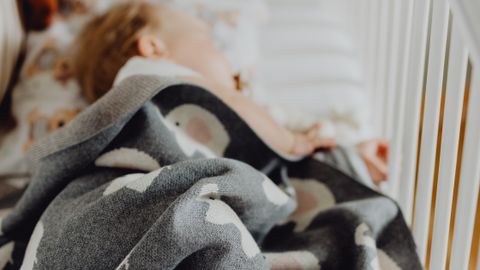 A baby sleeps peacefully in a crib with a cozy blanket and a teddy bear nearby.