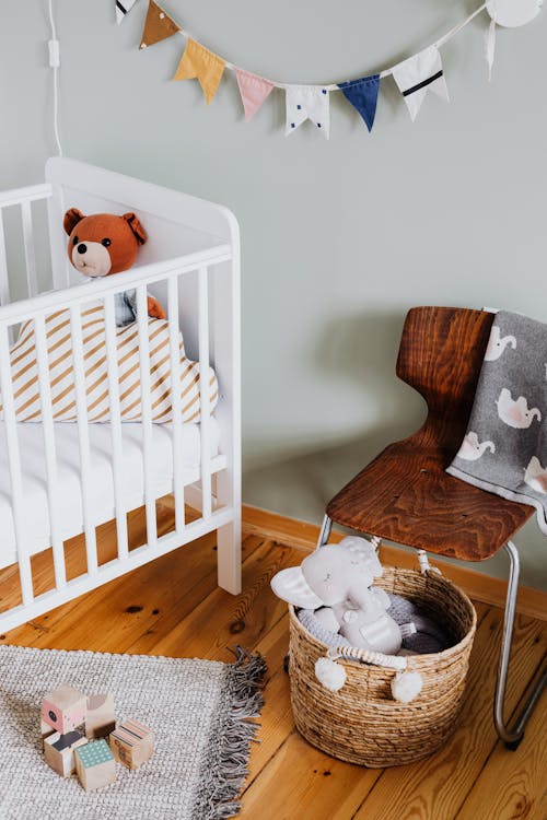 White Baby Crib beside a Wooden Chair 