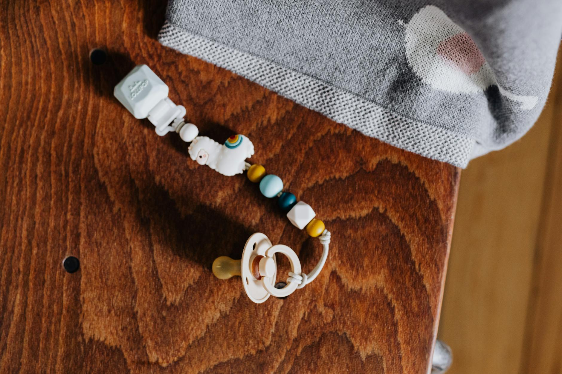 A vibrant baby pacifier clip with beads resting on a wooden surface.