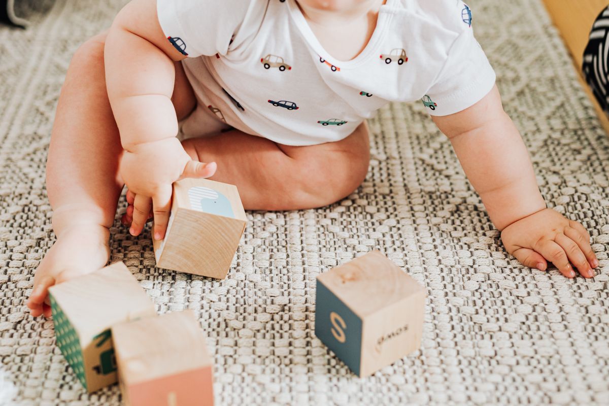 Baby playing with colorful wooden blocks on a soft carpet, practising fine motor skills