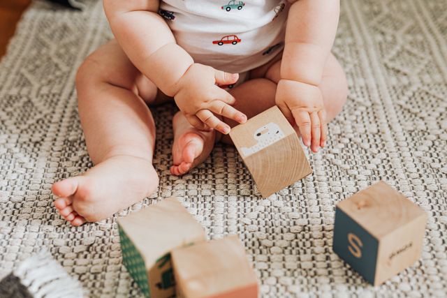 A baby playing with soft blocks on a rug