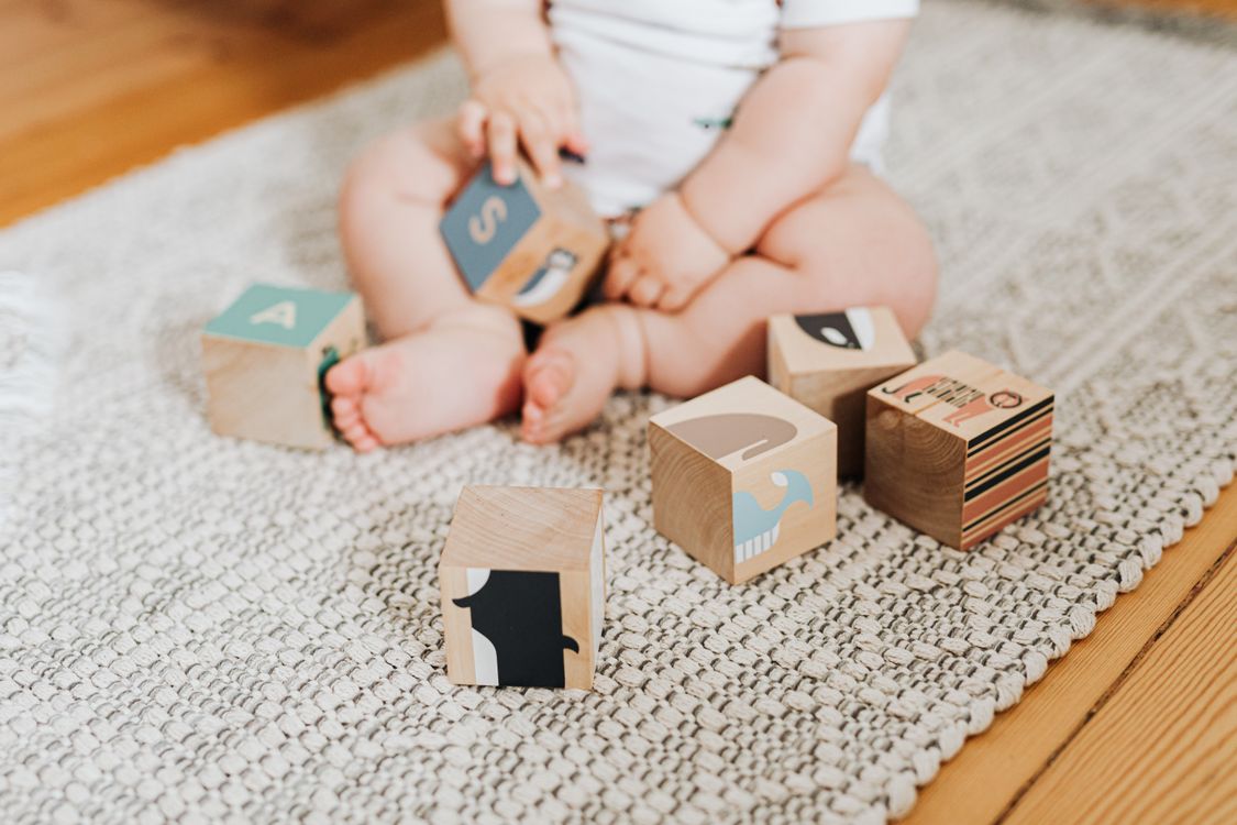 Bébé jouant avec des jouets Montessori en bois colorés sur un tapis, illustrant l'éveil bébé montessori.