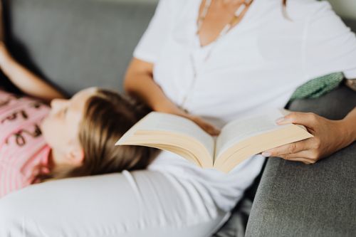 Free A woman reading with a child resting on her lap on a cozy sofa. Stock Photo