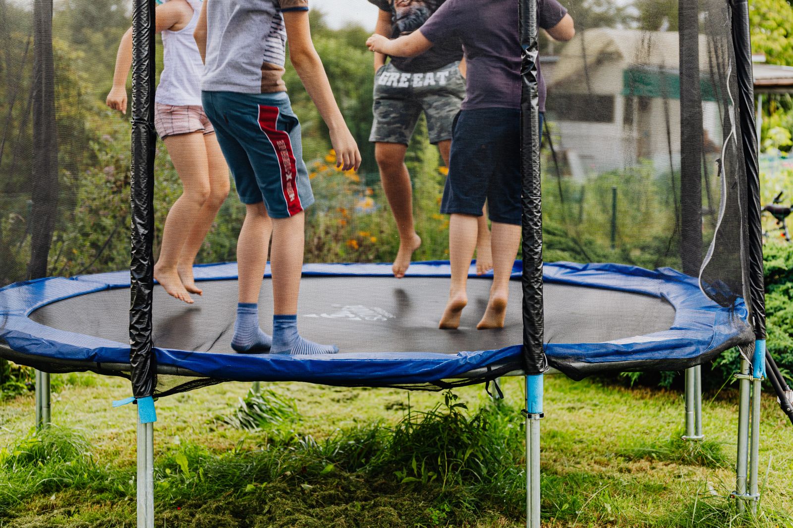 Four children bounce together on a netted trampoline in a backyard