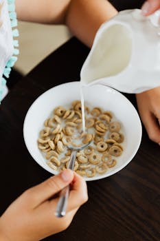 A close-up shot of milk being poured into a cereal bowl held by a child.
