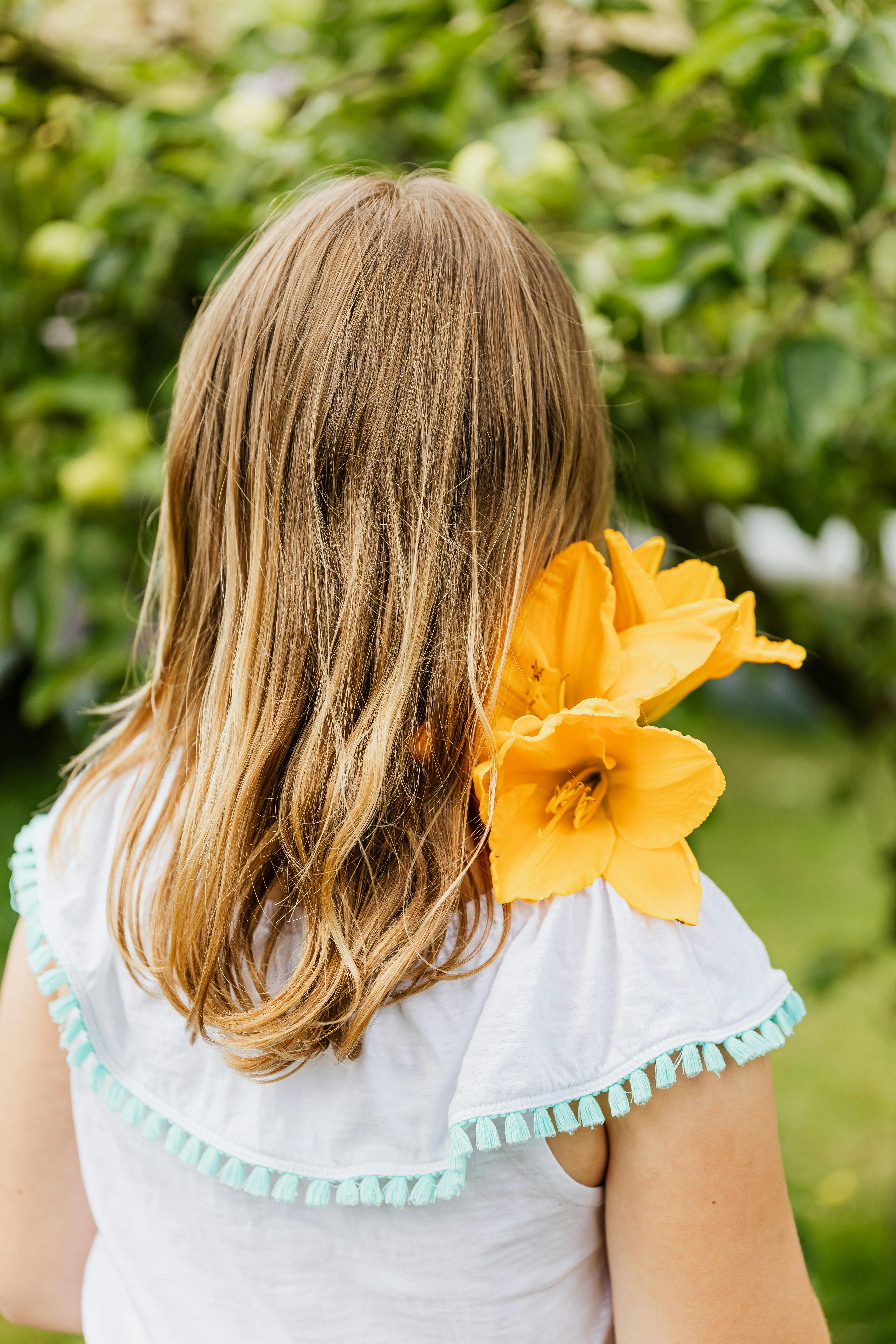一个年轻女孩，长着长发，戴着黄色花朵，站在绿色的花园里