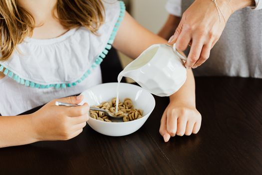 A close-up of milk being poured into a cereal bowl held by a child.