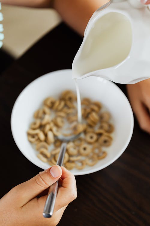 Person Pouring Milk on Ceramic Bowl with Cereals