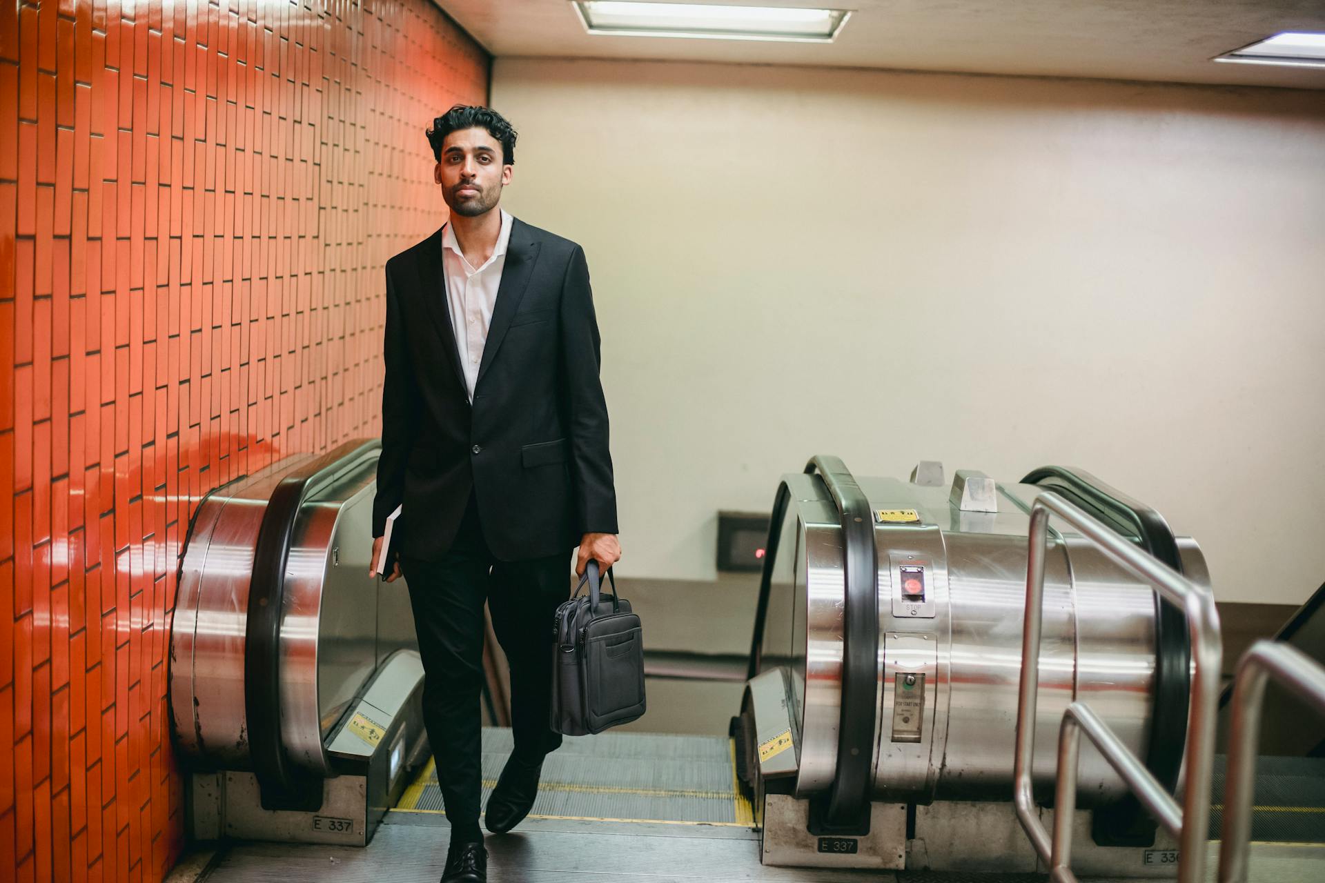 Man in a black suit with a briefcase and notebook on an escalator, subway setting.