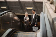 两名商务专业人士身着正装，在室内自动扶梯上互动