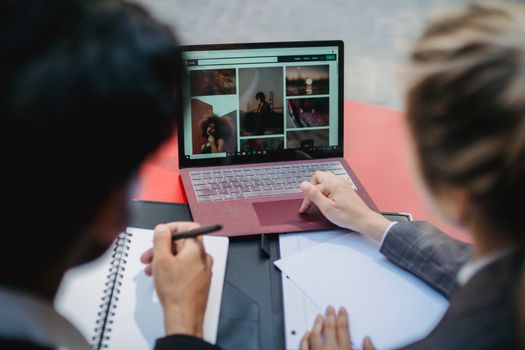 Two professionals working on a laptop at a table, discussing content and taking notes.