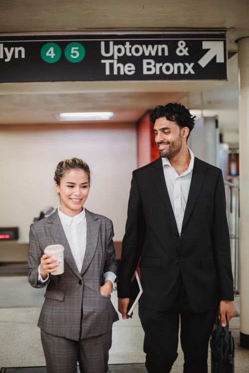 Free Two professionals in formal attire commuting, smiling and carrying coffee and bags. Stock Photo