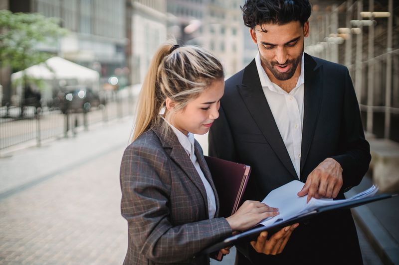 Two business professionals reviewing documents in an urban outdoor setting.