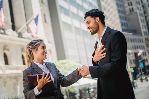 Free Professional man and woman handshake outside urban office setting with American flag in background. Stock Photo
