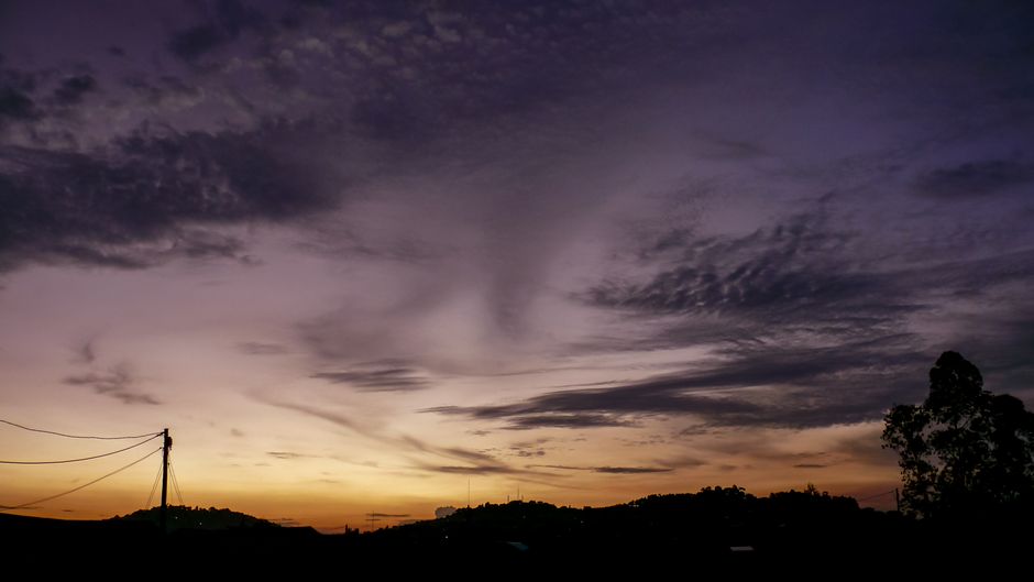 Dramatic sunset sky with purple hues and silhouetted trees over Kampala. Perfect for travel and nature themes.