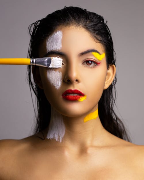 Woman covering eye with painting brush