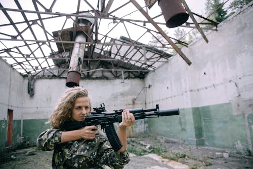 Woman in Green and Black Camouflage Jacket Holding a Long Black Rifle