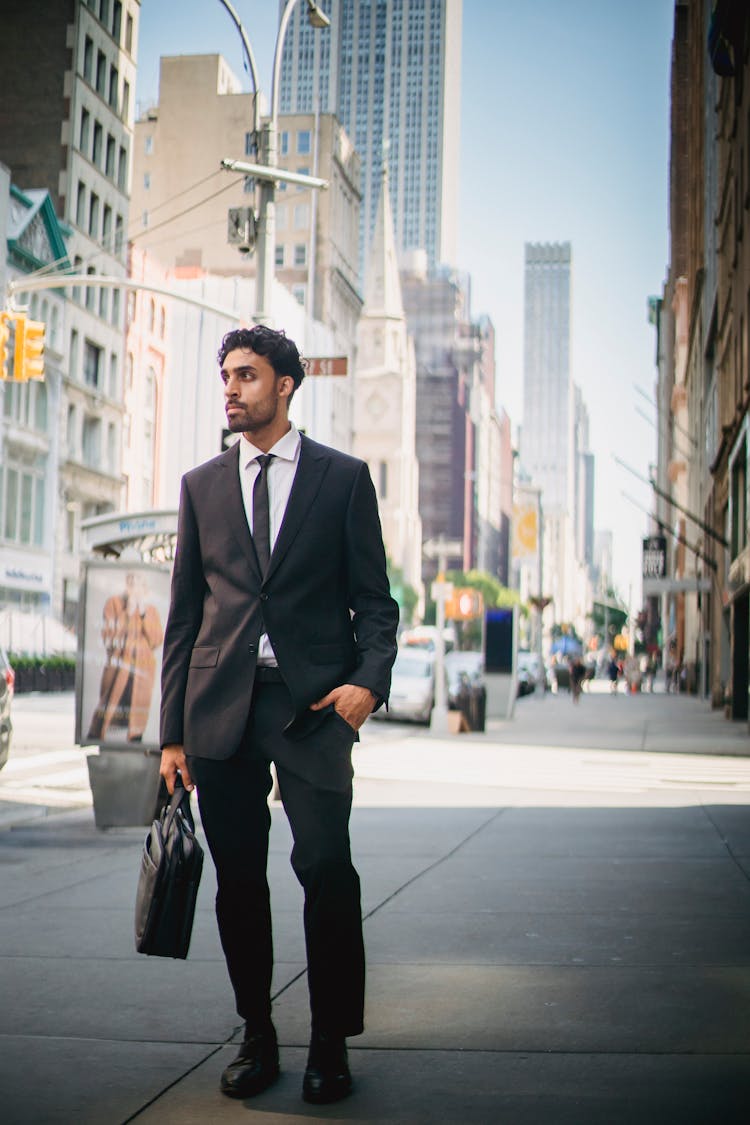 Man In Black Suit Jacket And Black Pants Standing On Sidewalk