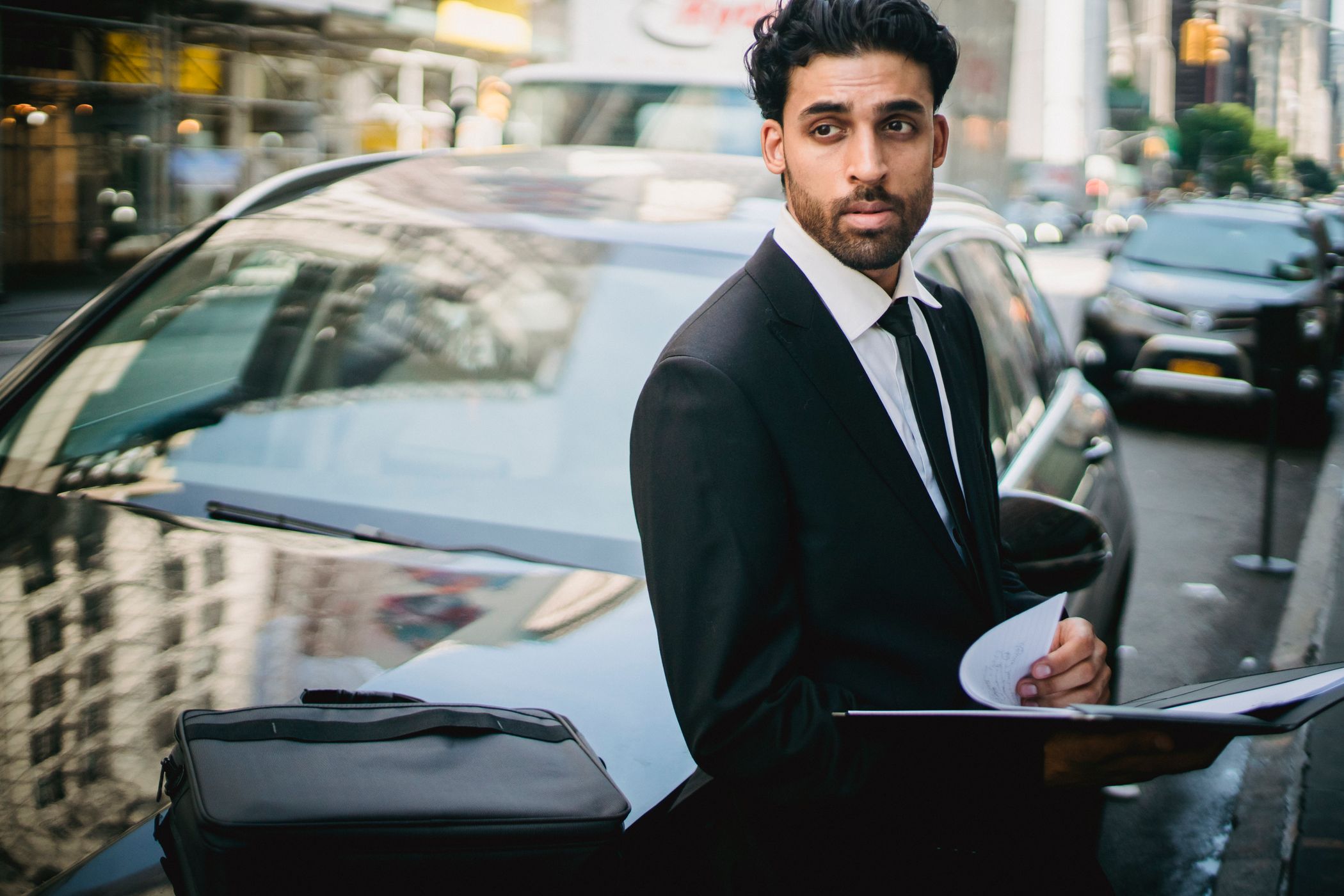 A chauffeur standing at the open door of a black luxury car