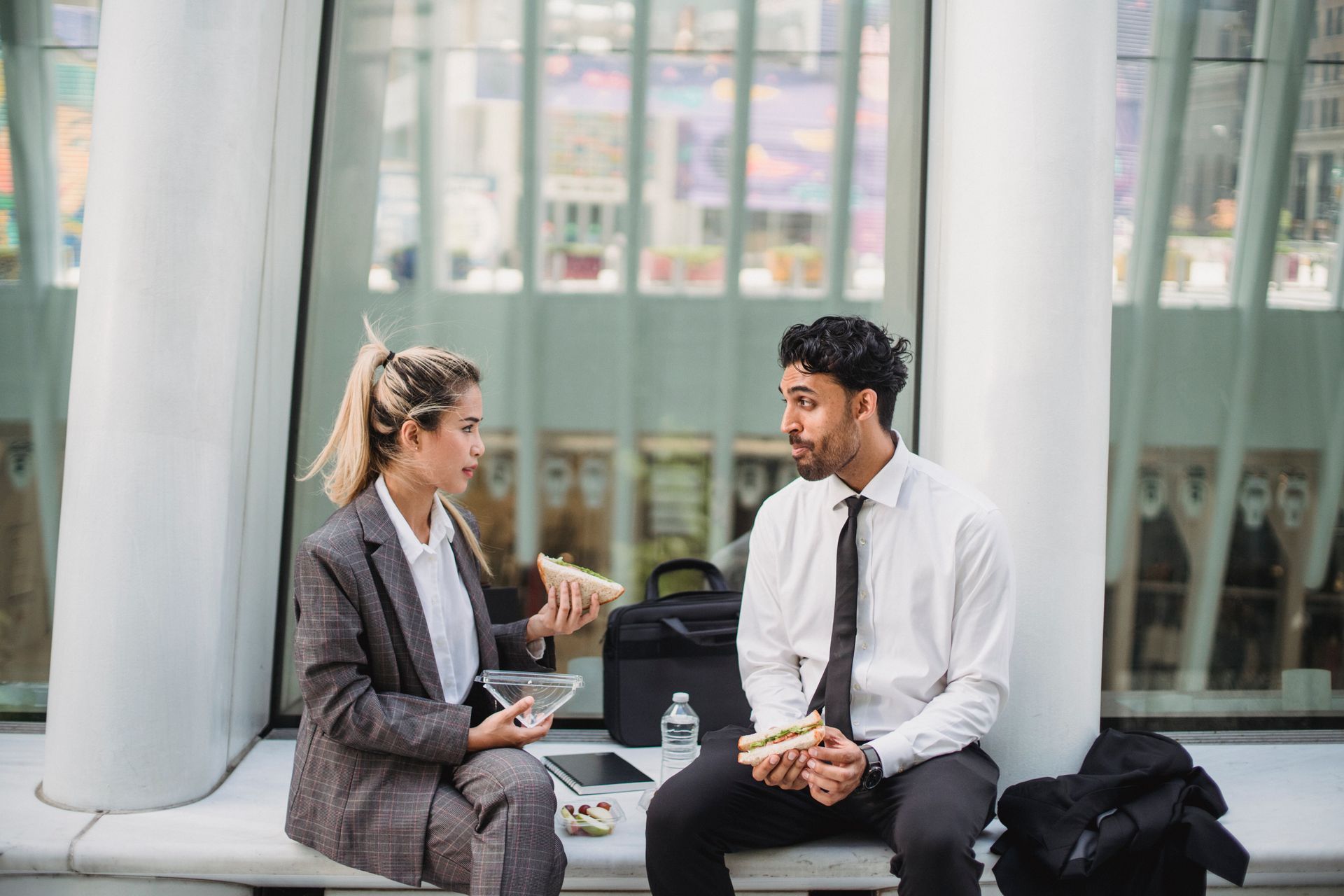 Two professionals in a modern office enjoying a lunch break and engaging in conversation.