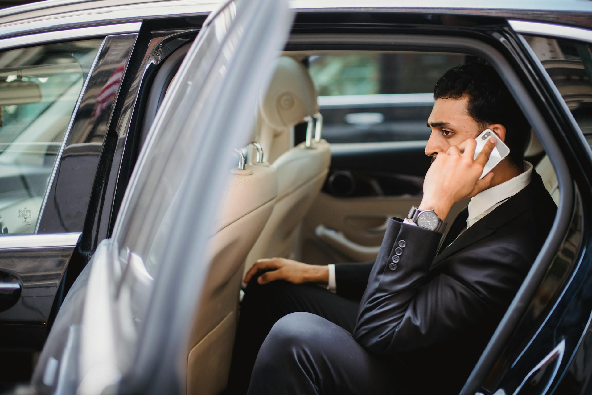 Professional man in suit making a phone call while sitting in a vehicle.