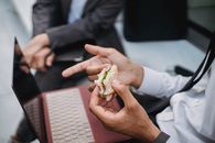 一位专业人士在工作休息期间拿着三明治，附近放着一台笔记本电脑