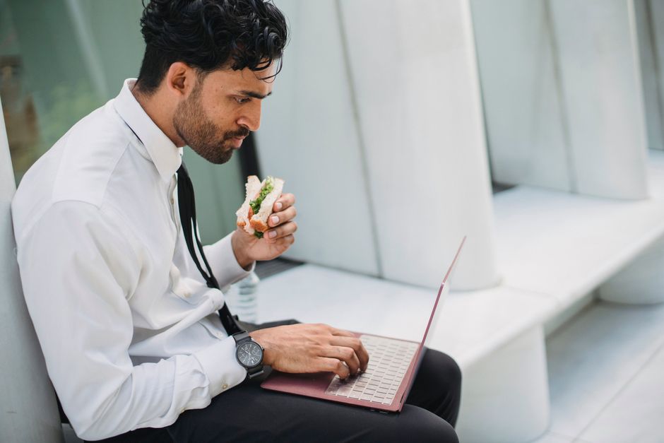 Businessman eating a sandwich while working on a laptop outdoors. Perfect for lifestyle or business themes. Businessman eating a sandwich while working on a laptop outdoors. Perfect for lifestyle or business themes.