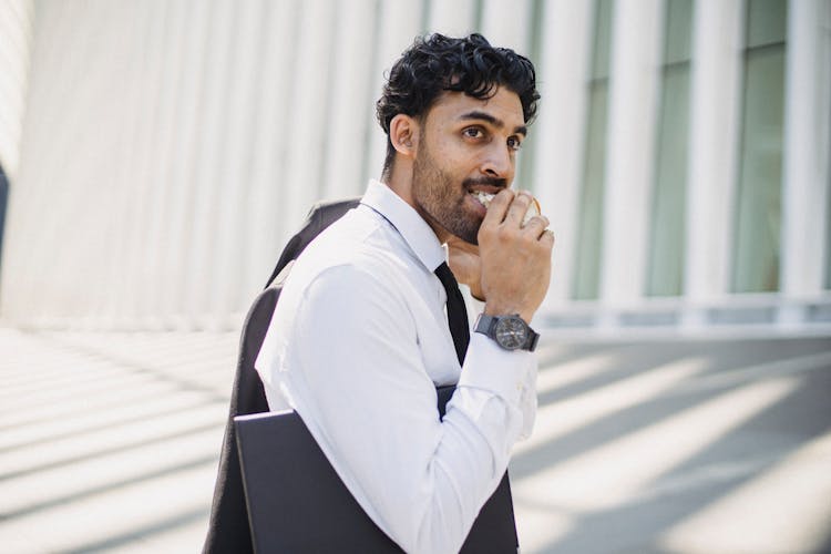 
A Bearded Man In A Corporate Attire Eating A Sandwich