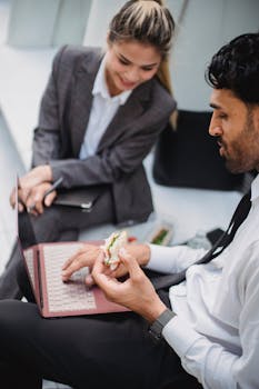 A man and woman having a business meeting outside, engaging with a laptop while eating.