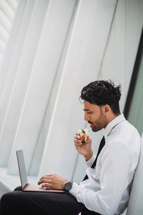 Free 
A Bearded Man in a Corporate Attire Eating while Using His Laptop Stock Photo