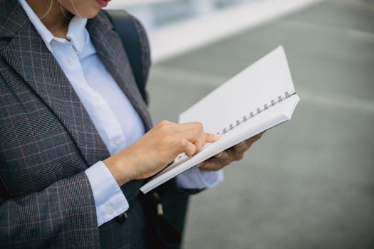Close-up of a professional woman in a blazer writing in a notebook outdoors.