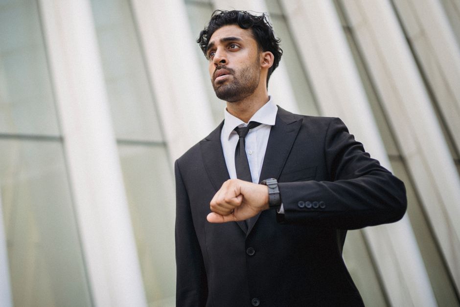 Hombre de negocios en traje revisando la hora en un reloj, de pie junto a una arquitectura moderna.