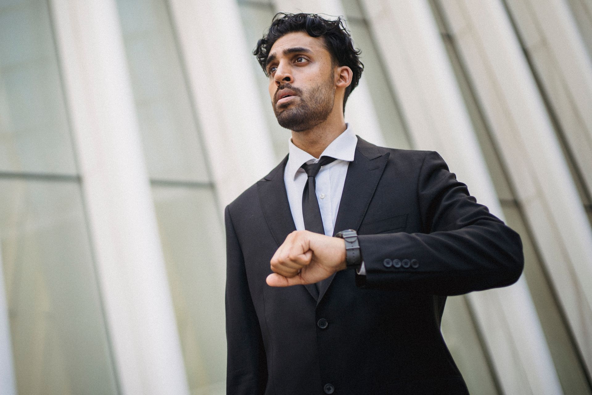 Businessman in suit checking time on watch, standing by modern architecture.