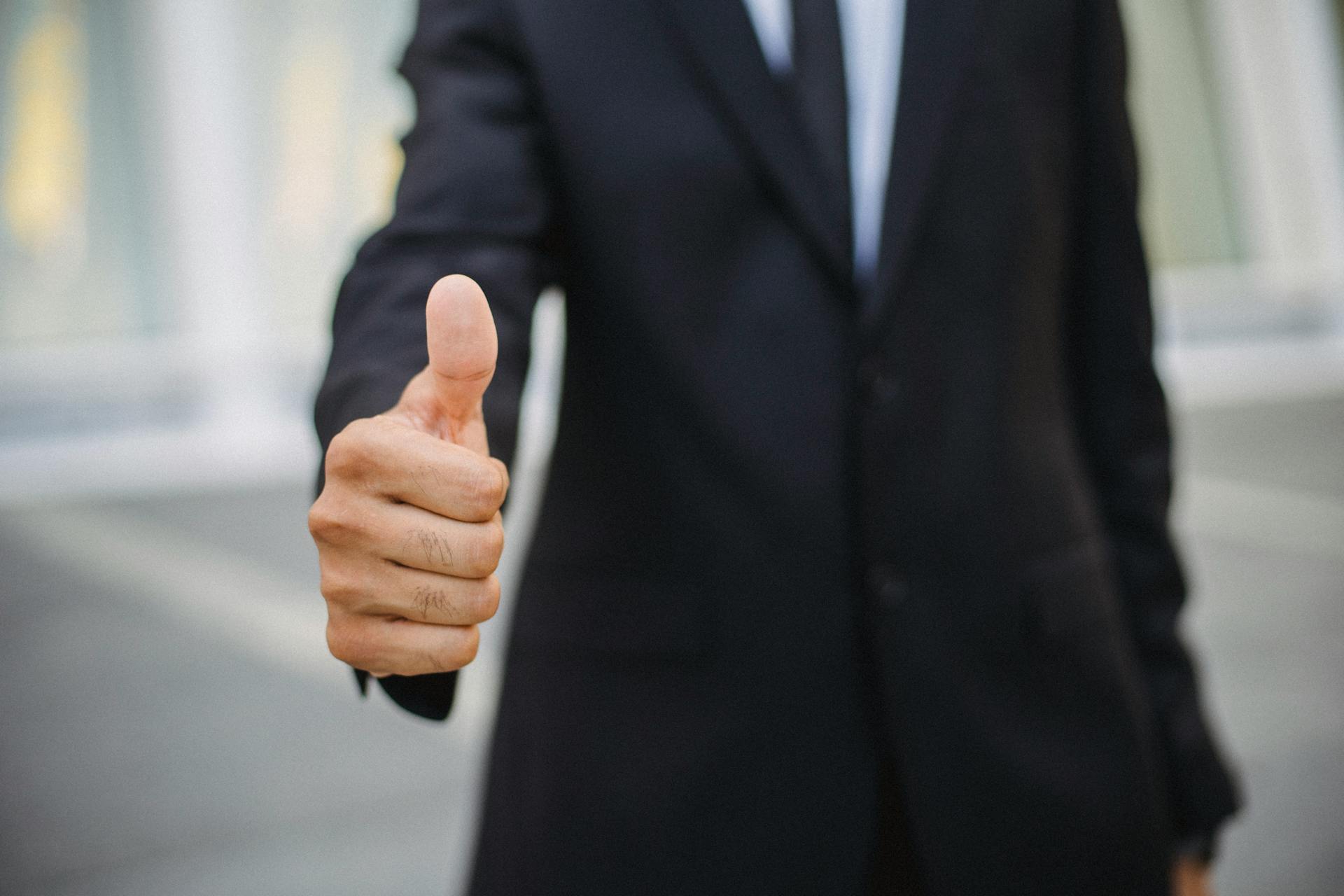 Close-up of a businessman in a suit giving a thumbs up gesture, symbolizing approval.