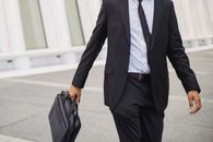 一位西装革履的商人提着公文包，自信地走在户外，展现了企业的专业精神