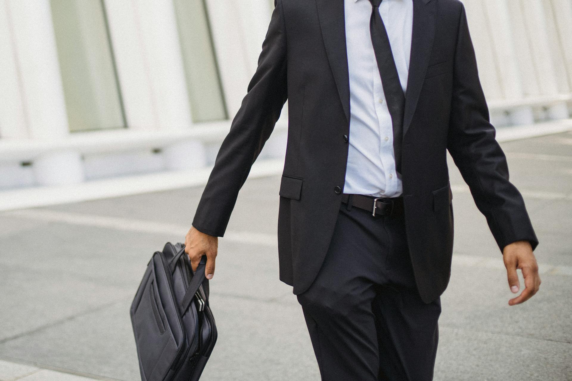 A businessman in a suit carrying a briefcase walks confidently outdoors, showcasing corporate professionalism.